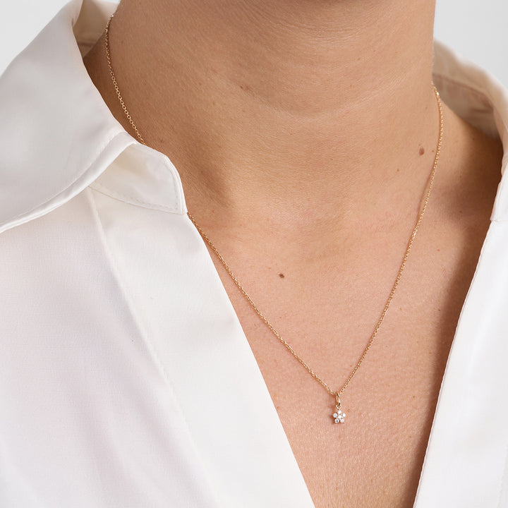 Guldhalsband med litet blomformat hänge och diamanter, framsida på modell