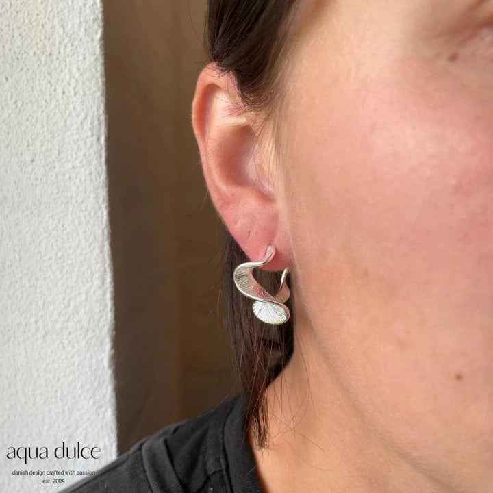 Aqua Dulce Rhumba Medium Hoop i silver syns på örat, elegant vågig design. Modell 5319-5319-2