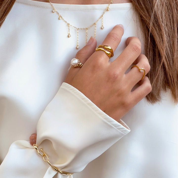 Aqua Dulce Wave Ring i guldpläterad sedd till hands med andra ringar, elegant och organisk design. Modell 6626-001