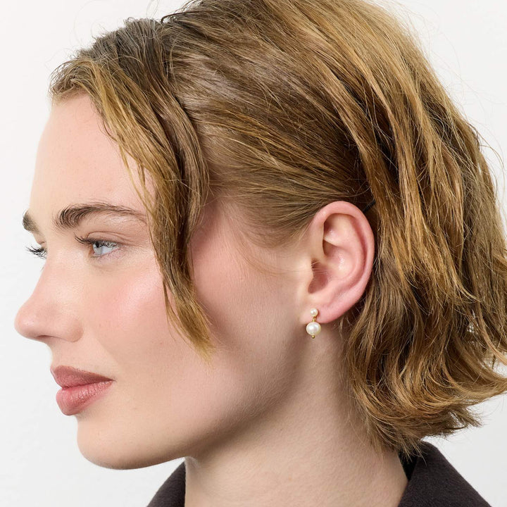 carre-sally-guldpläterade-malmstickor-med-sötvattenspärlor visas på modell, krämfärgad pärla och gulddetalj. Modell FS4582BI-BI-2