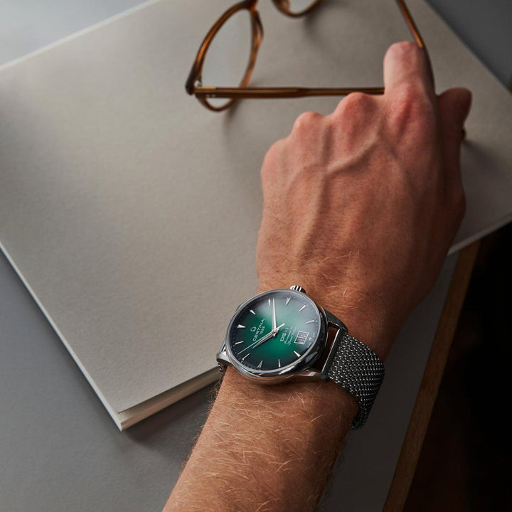 Certina DS-1 Big Date grön urtavla med stålnätsrem som bärs på handleden vid skrivbordet. Modell C0294261109160