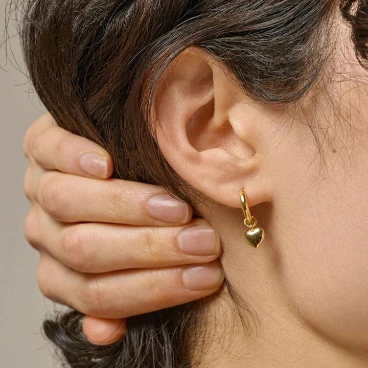 Enamel Amore Gilded Hoops visar ett guldpläterat hjärtörhänge i örat på en kvinna. Modell e376g-e376g-2