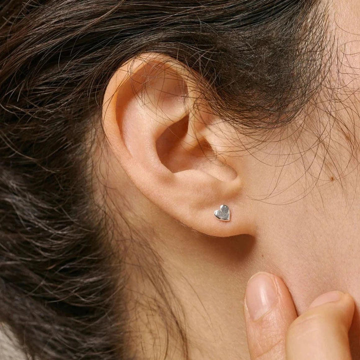 Enamel Heart Studs visas som silverfärgade hjärtörhängen i modellens öra, eleganta och minimalistiska. Modell E373SM-E373SM-2