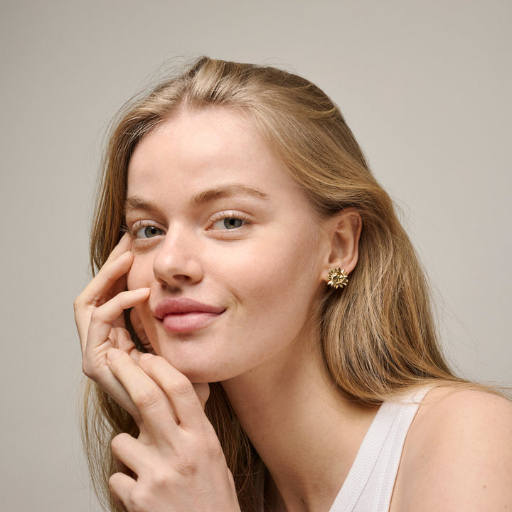 Enamel Stor Sunshine Stud visad på modell, gyllene solformade dubbar i örat. Modell e421g-2