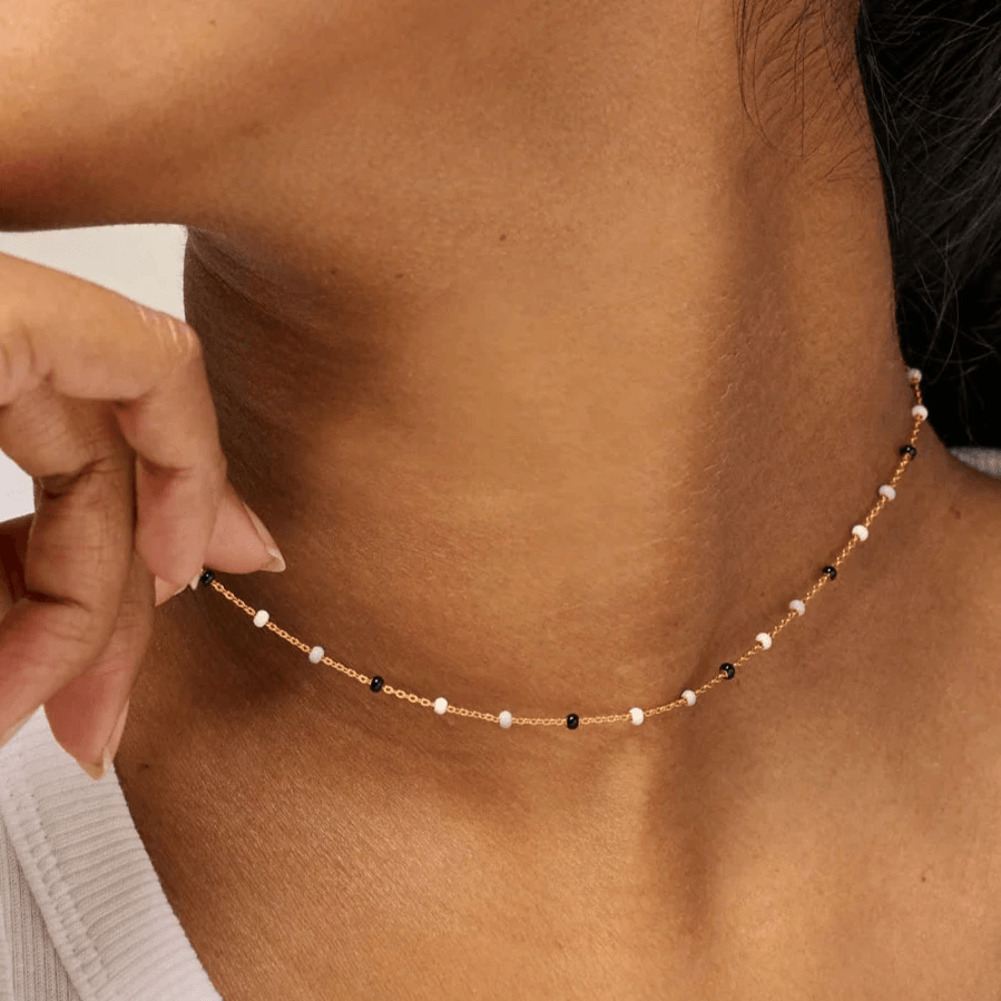 Enamel Lola Salt n Pepper Halsband visas runt modellens hals, tunn kedja med små vita och svarta pärlor. Modell N55G-SALT PEPPAR