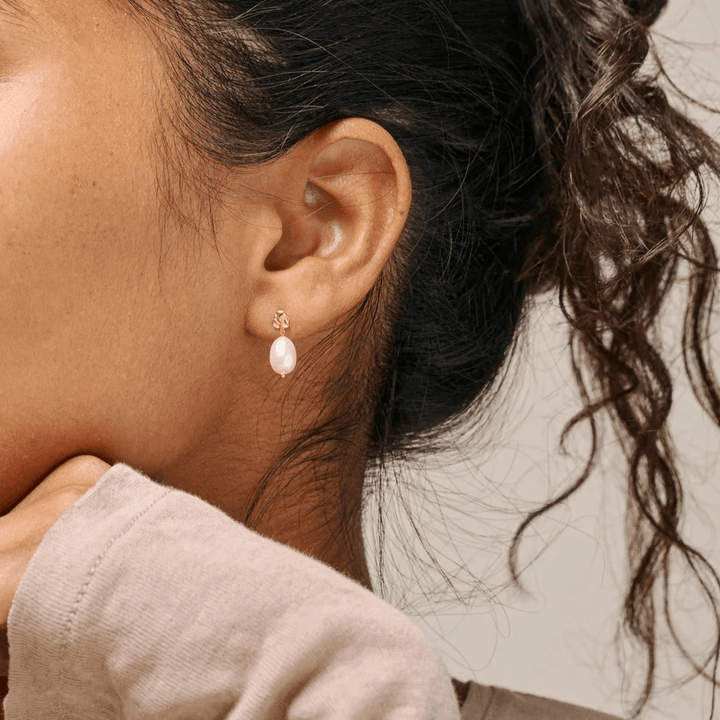 Enamel Poe Pearl Studs visas här bärs på örat, elegant sötvattenspärla och guldton detalj. Modell e384gm-pearl