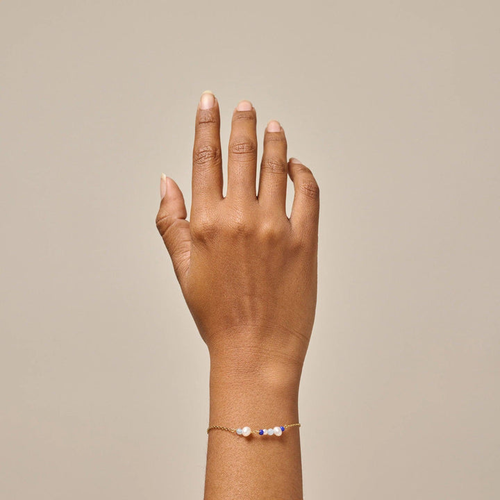 Enamel Sofia Armband Marine visas bärs på handleden, gyllene kedja med vita och blå pärlor. Modell b136g-marine