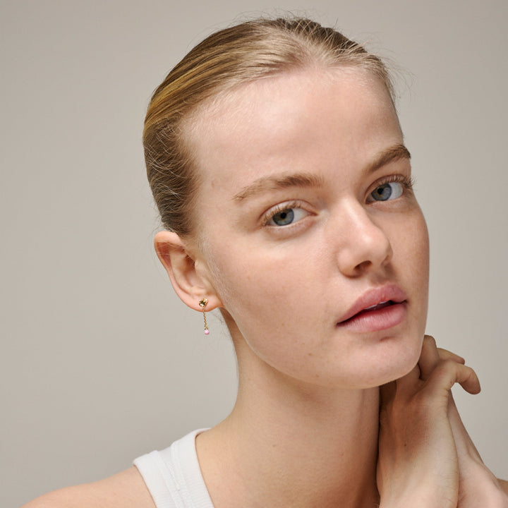 Enamel Sunshine Drop Earrings Rosa kan ses på modellen med uppsatt hår. Guldfärgade örhängen med rosa detalj. Modell e423g-rosa-2.