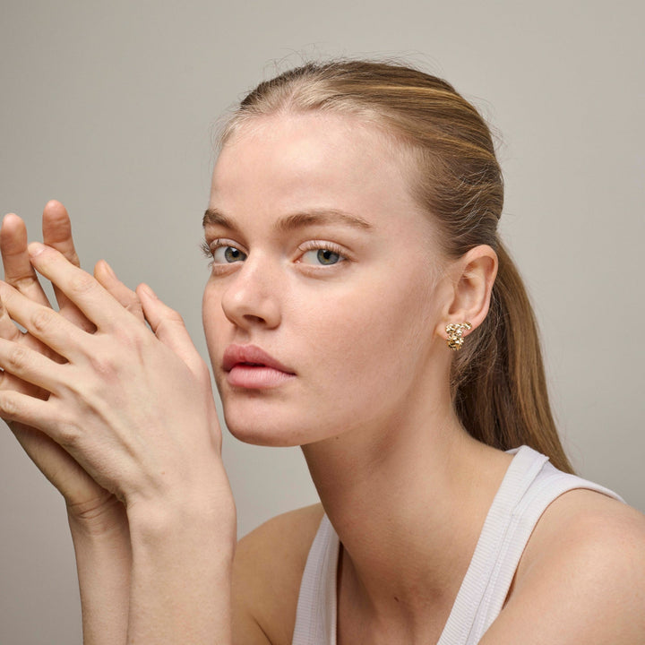 Enamel Sunshine Field Stud e417g visas bärs av en kvinna, gyllene örhängen i en organisk form. Modell e417g-2