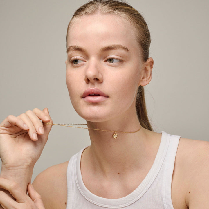 Enamel Sunshine Necklace Daisy n136g dyker upp på nacken på modellen, guldkedja med litet blomhänge. Modell n136g-daisy-2