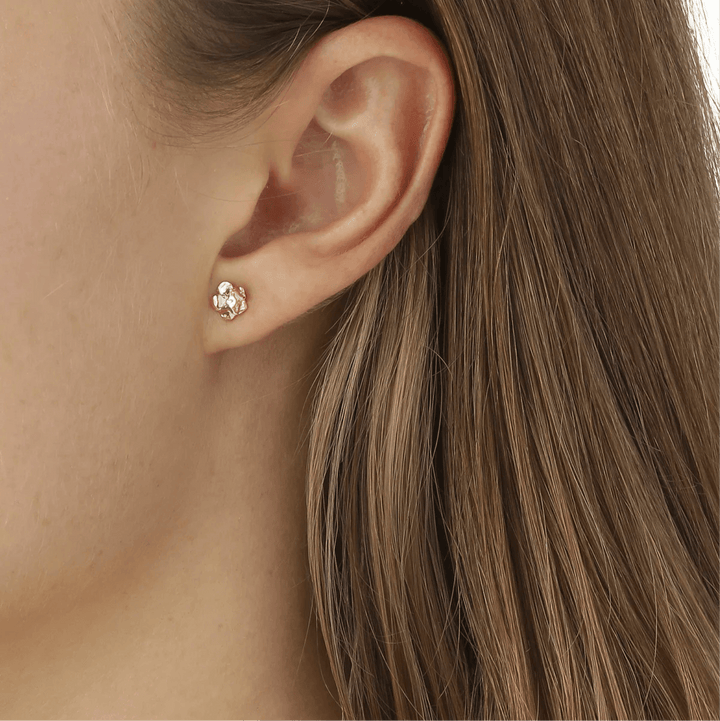 Flora Danica Glöm små öronknäppar 18 karat guld som visas på örat, detaljerad blomdesign. Modell fmn-stpc-18k-g-2