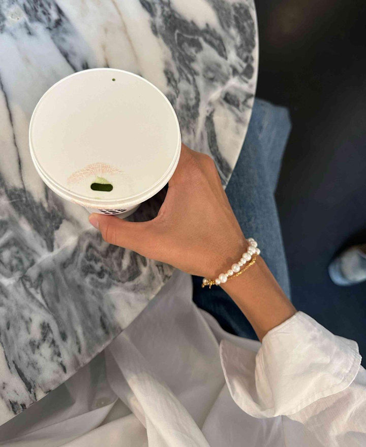 Hultquist Copenhagen Josephine armband med vita pärlor och gulddetaljer bärs till hands, modell S08559G-2.