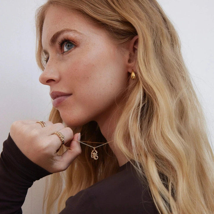 Jeberg I AM Zodiac halsband guldpläterad zodiac som bärs av kvinna med vågigt ljust hår. Modell 42400-001.