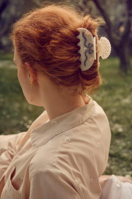 maanesten-desiree-hår-klo-benvitt ses i kvinnans stylade röda hår, i en solig utomhusmiljö. Modell 3973-one size