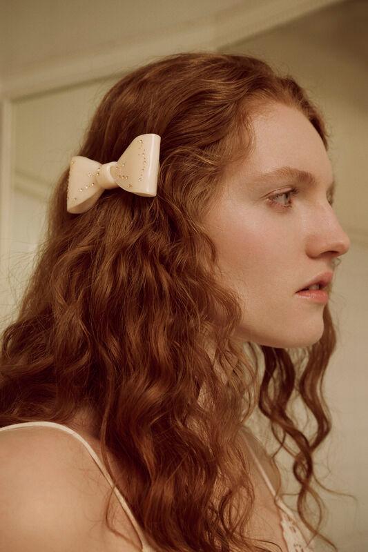 Maanesten Ribin Hair Clip Cream visar en krämfärgad hårklämma i rosettform på långt lockigt hår. Modell 3981