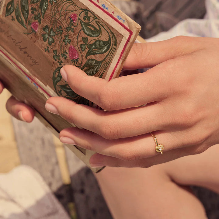 Maanesten Tacita Ring guldpläterad sedd till hands i solljus, enkel blomring i guldlook, modell 4882a-001