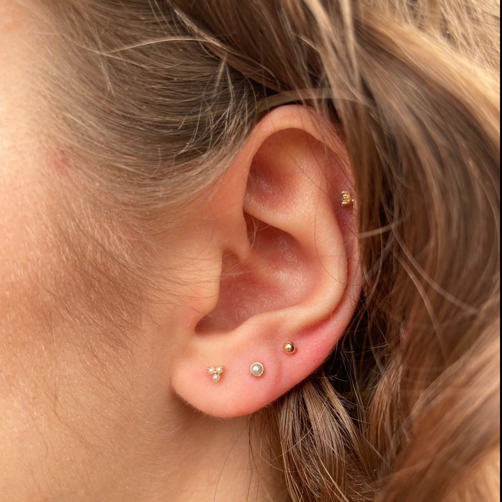 Maria Tash Natural Pearl Threaded Stud Örhänge 14kt visas i ett öra, diskret sötvattenspärla på guld. Modell xpe-yg-w2-001-2.