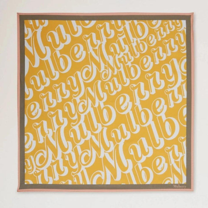 Mulberry Fantasy Logo Square Scarf visar en gul halsduk med vit Mulberry- tryck och rosa kant. Modell VS4802027P504