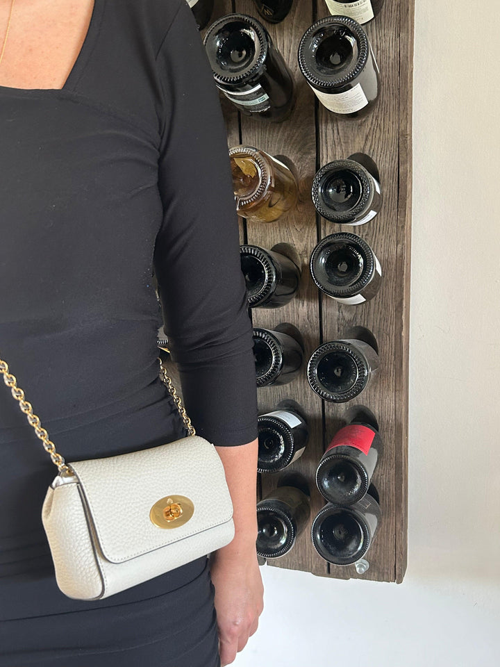 Mulberry Mini Lily Heavy Grain Chalk, sliten crossbody på kvinna i svarta kläder, framför vinställ. Modell rl7944736w160-2