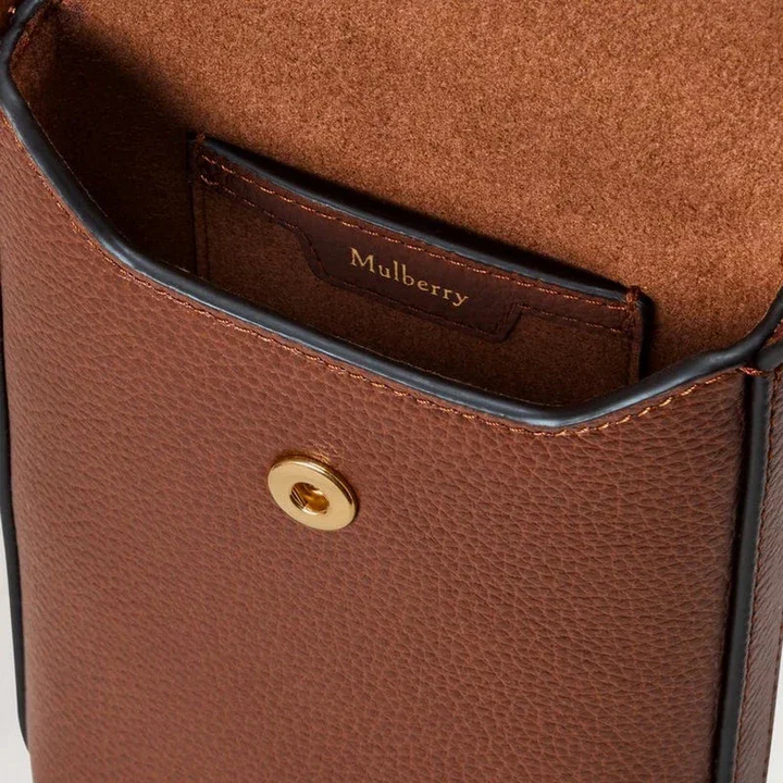 Mulberry Press Stud Phone Pouch ek som visar närbild av brun läderyta och guldfärgad tryckknapp, modell RL9007552G110