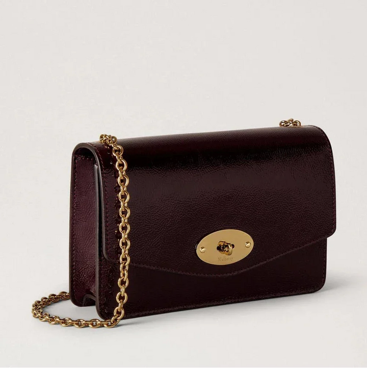 Mulberry Liten Darley Deep Aubergine Patent visar en liten, glänsande axelväska i mörkt aubergineläder med en gyllene kedjerem. Modell RL8922737V697
