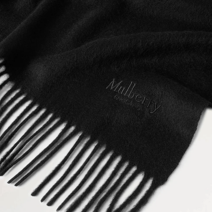 Mulberry Solid Merino Wool Scarf Black visar en svart merinoullscarf med fransar och diskret logga. Modell vs4240947a100