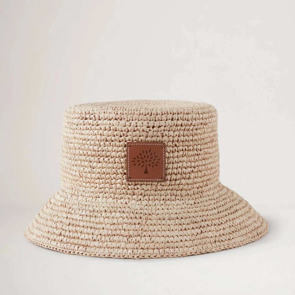 Mulberry Summer Raffia Bucket Hat visar upp en ljus flätad raffia-sommarhatt med läderdetalj framtill. Modell VH4097807H120