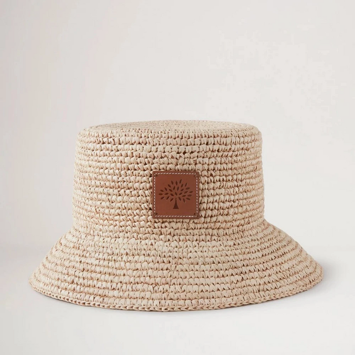 Mulberry Summer Raffia Bucket Hat visar upp en ljus flätad raffia-sommarhatt med läderdetalj framtill. Modell VH4097807H120