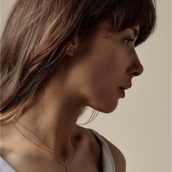 Nuran 14kt Zoe örhängen visas diskret på en kvinnas öra, enkla och eleganta i guld. Modell o2314-006rg-2.