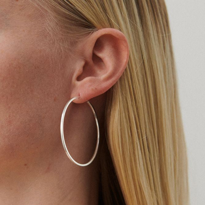 Pernille Corydon Orbit Store Hoops i silver visas bära i örat på en modell med ljust hår. Modell E-053-S
