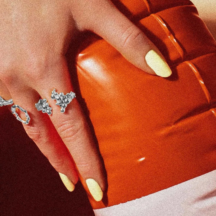 Vincent Orb Chronicles Solv Ring, elegant silverring med organisk design till hands med ljusa naglar framför orange bakgrund. Modell VJ163-URS-001-2