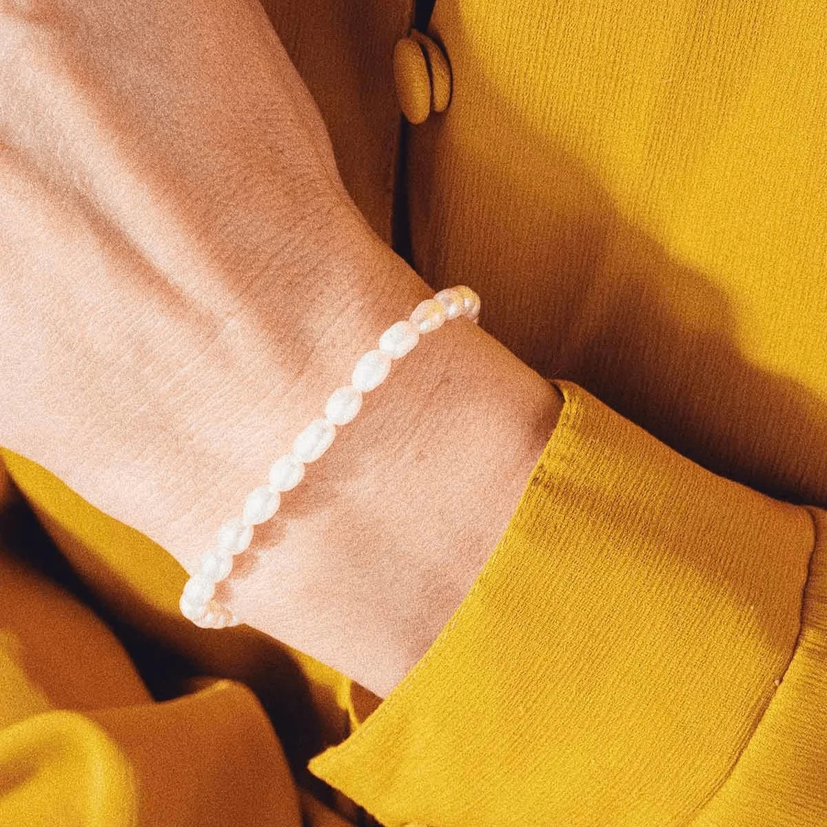 Vincent Venus Armband med förgyllda pärlor bärs runt handleden, vita pärlor syns tydligt. Modell VJ082-UBG-1