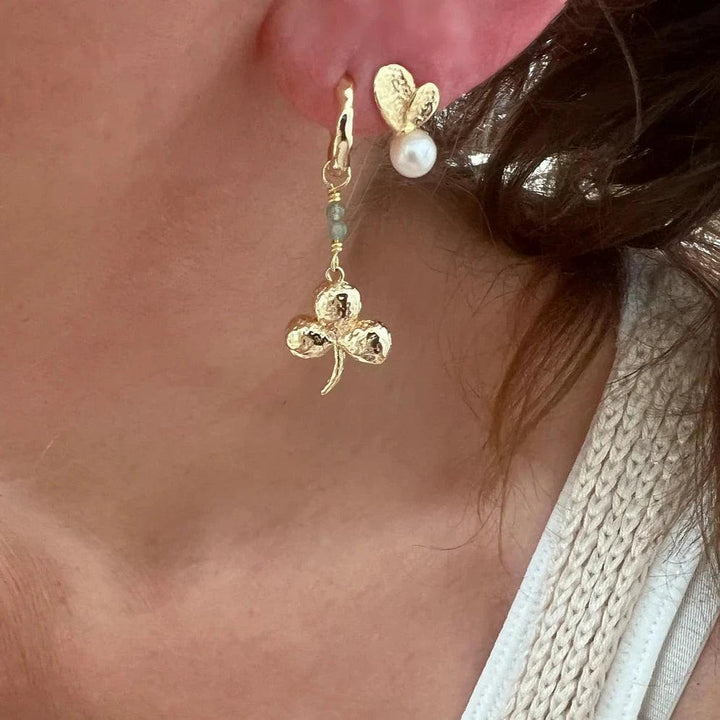 Wioga Madison örhängen med trefoil, guldfärgade med pärldetalj, ses på örat. Modell E-8905-gp.