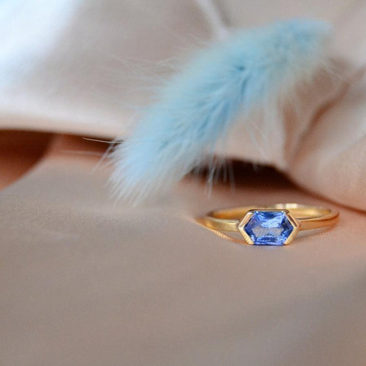 anpe-atelier-anpassad-ring-med-blå-safir visas på beige tyg, sexkantig blå safir i guld. Modell27-blasafir-001-2