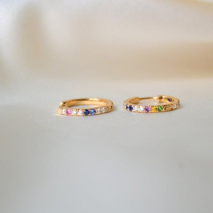 anpe atelier kyra creoles 18kt guld med briljanter och ädelstenar, två örhängen med färgade stenar liggande på en ljus bakgrund. Modell 23-2-anpassad-1