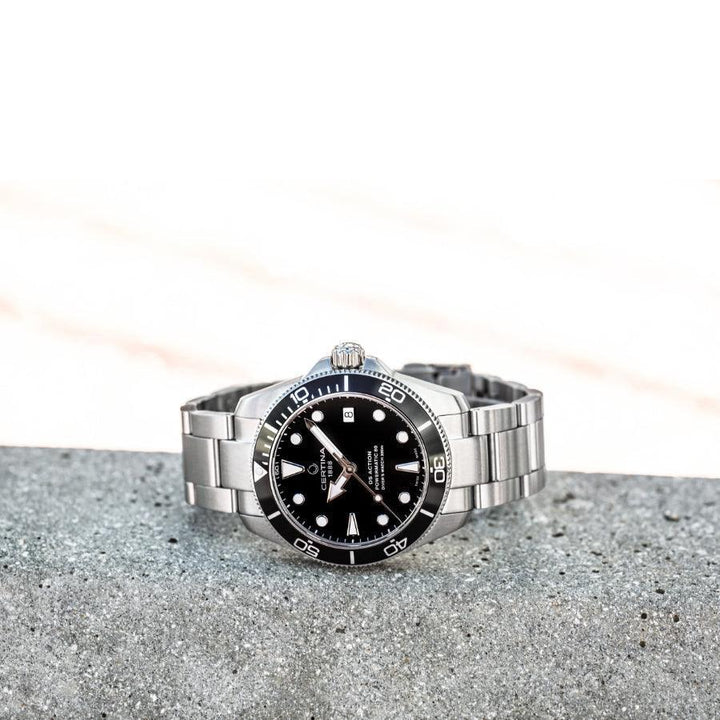 Certina DS Action Powermatic 80 herrklocka med svart urtavla med stålkedja på grå betong, modell C0328071105100.