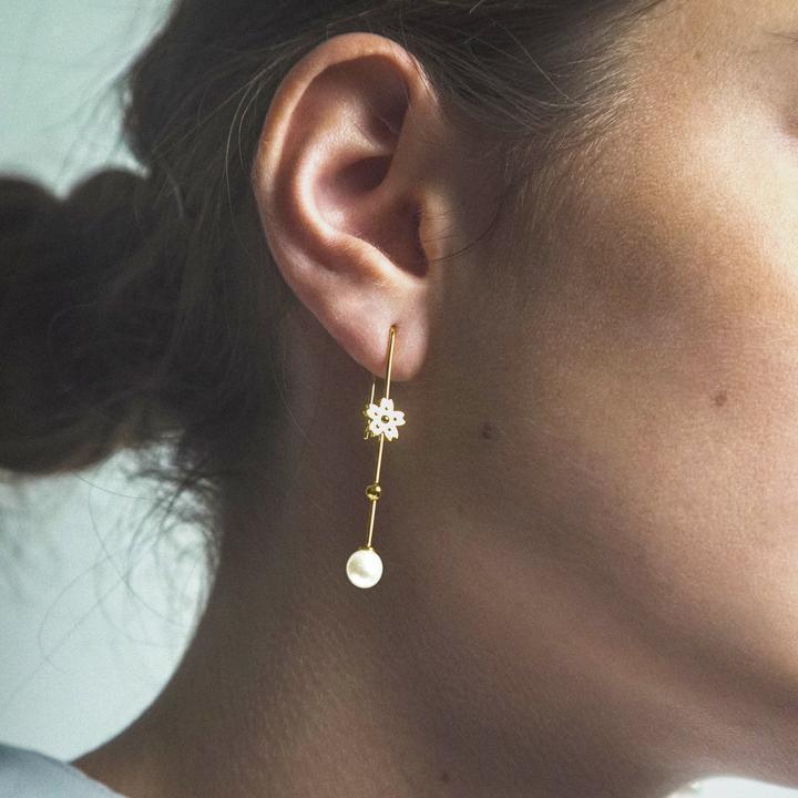 Polar Jewelry Sakura Hanging Pearl guldpläterat örhänge ses på örat, med guldblomma och pärla. Modell SAK-EH-GD-WP-00120