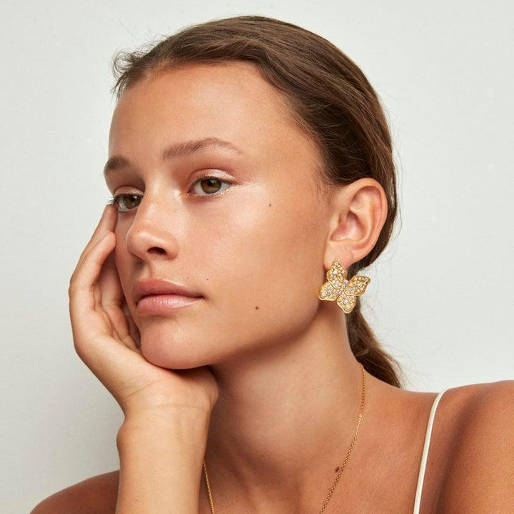 Polar Jewelry The Butterfly guldpläterat örhänge visas på örat, stor guldfärgad fjäril med stenar, modell TBU-ST-GD-WZ-00323