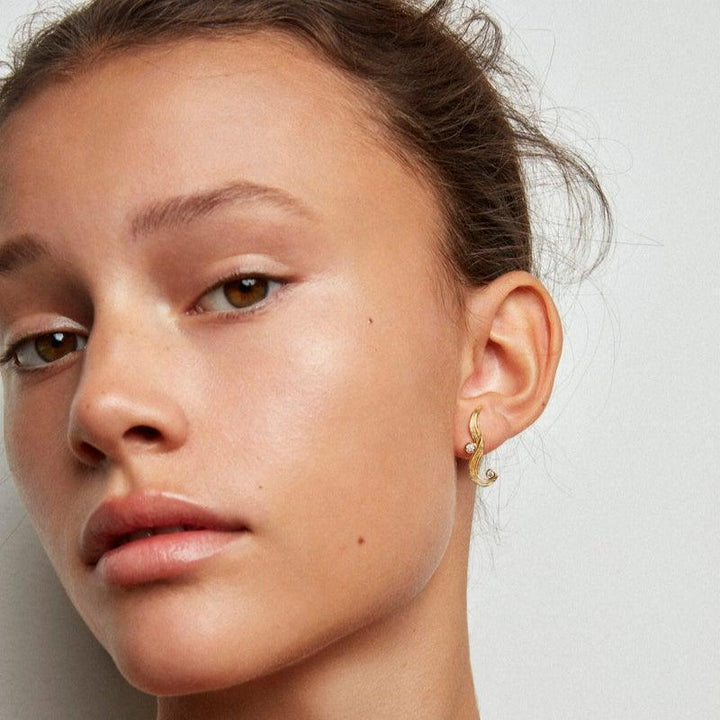 Polar Jewelry The Darning Needle guldpläterat örhänge på kvinnors öra, elegant böjd design. Modell dan-st-l-gd-wz-00331-2